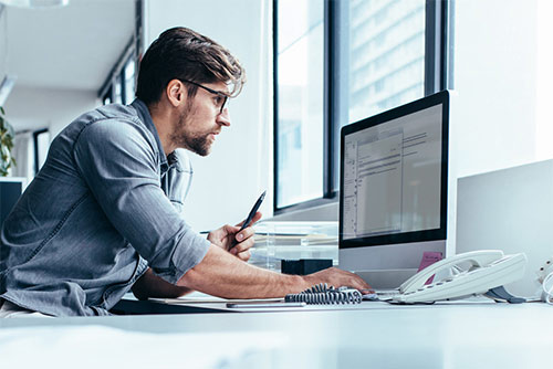 Man staring intently at a monitor with a pen in one hand